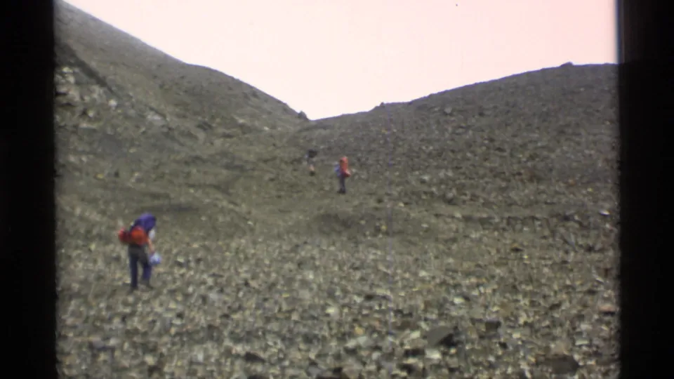1977 Alaska frame with small backpacked hikers on a rugged hillside, filmed from a handheld 8mm viewpoint.