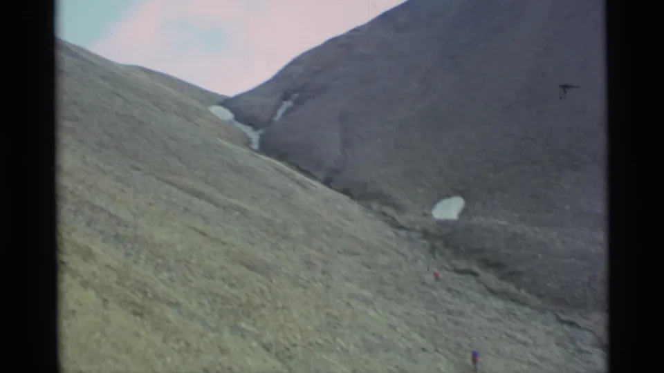 1977 Alaska home-movie frame of a broad mountain slope with snow remnants and a small climber near the bottom edge.