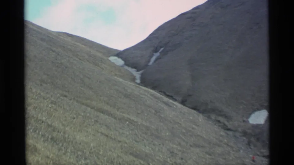 1977 Alaska 8mm frame looking across a steep mountain slope toward snow caught in a dark rocky gully.