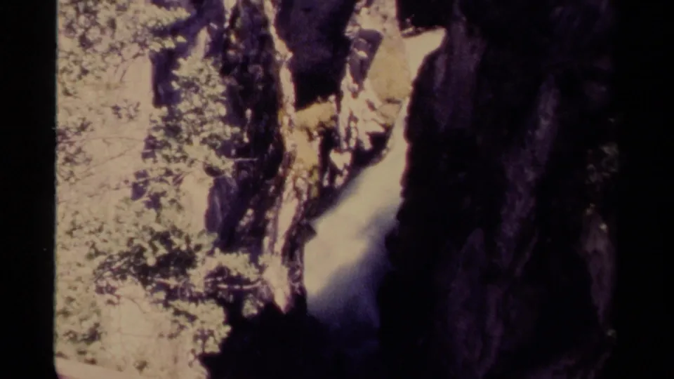 1979 Canadian 8mm frame showing a narrow waterfall in a rocky canyon with bright foliage and deep shadow.