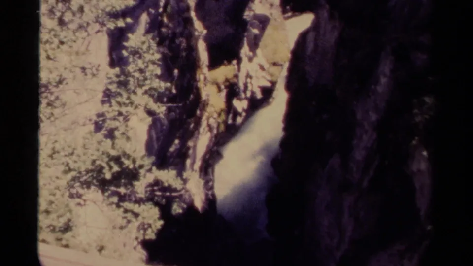 1979 Canadian 8mm view of water descending through a shaded canyon beside sunlit forest growth.