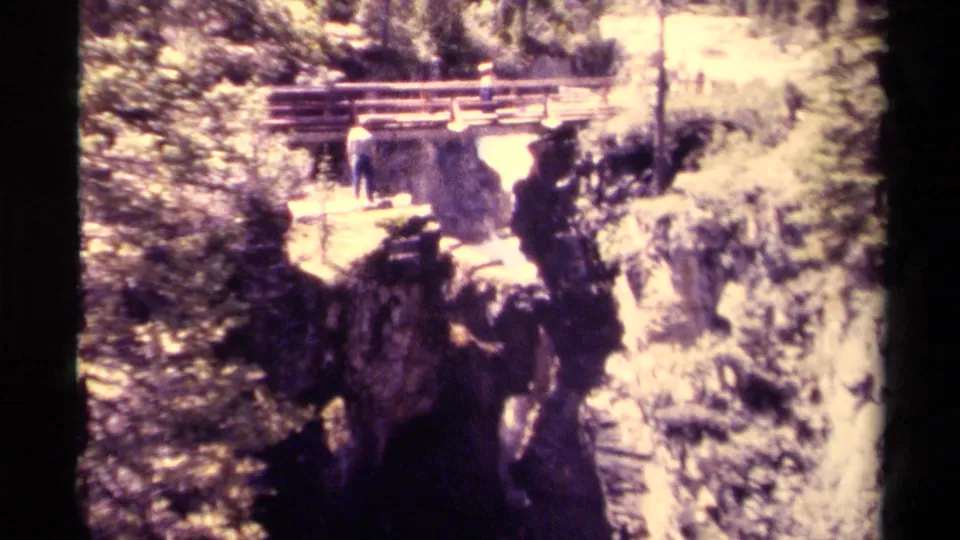 1979 Canadian 8mm frame showing a wooden observation bridge over a rocky canyon with small visitors near the waterfall viewpoint.
