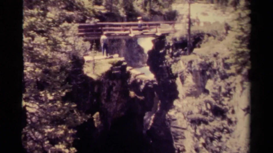 1979 8mm Canada home-movie frame showing a man beside a wooden bridge overlooking a steep rocky canyon and waterfall.