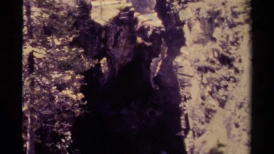 A soft, faded 8mm frame shows the canyon from above, with trees, pale rock, and the waterfall area in deep contrast.