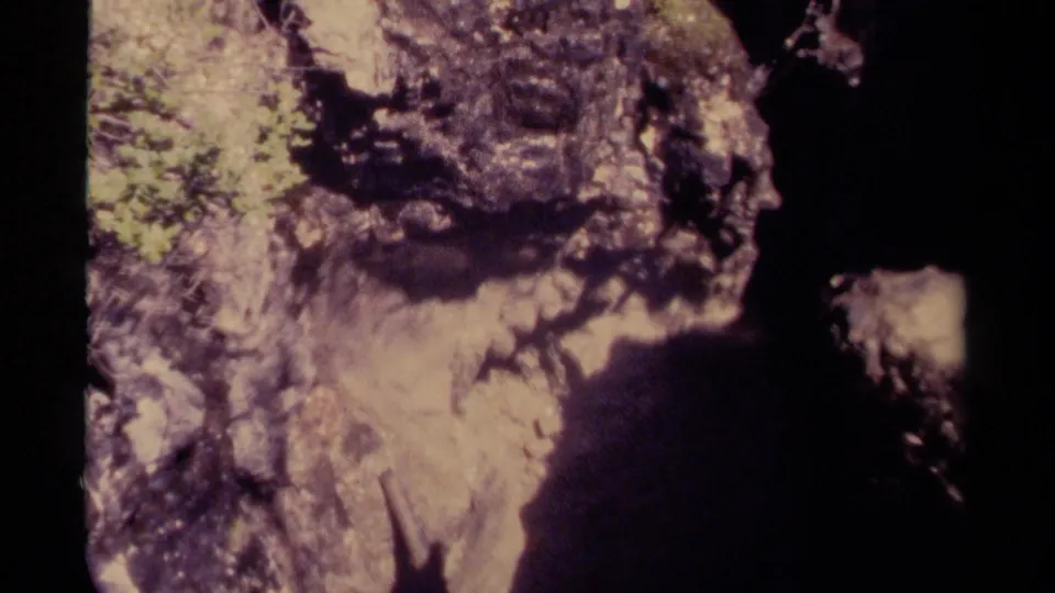 1979 Canadian 8mm frame looking down along a rugged rock face near the shadowed entrance of a cavern.