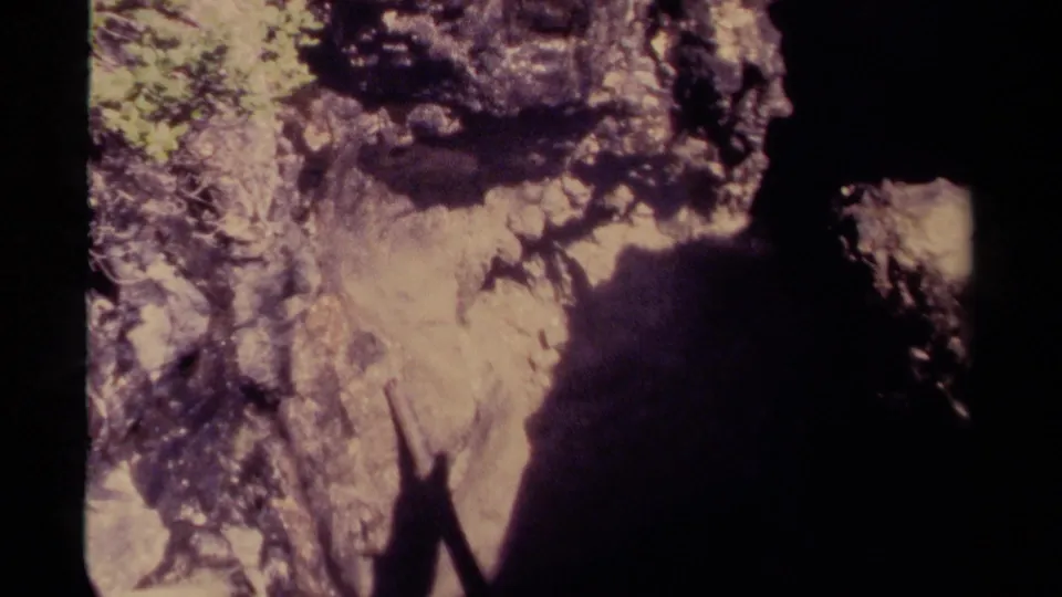 1979 Canadian 8mm frame showing a dark cave edge, rugged rock texture, and small green growth in natural light.