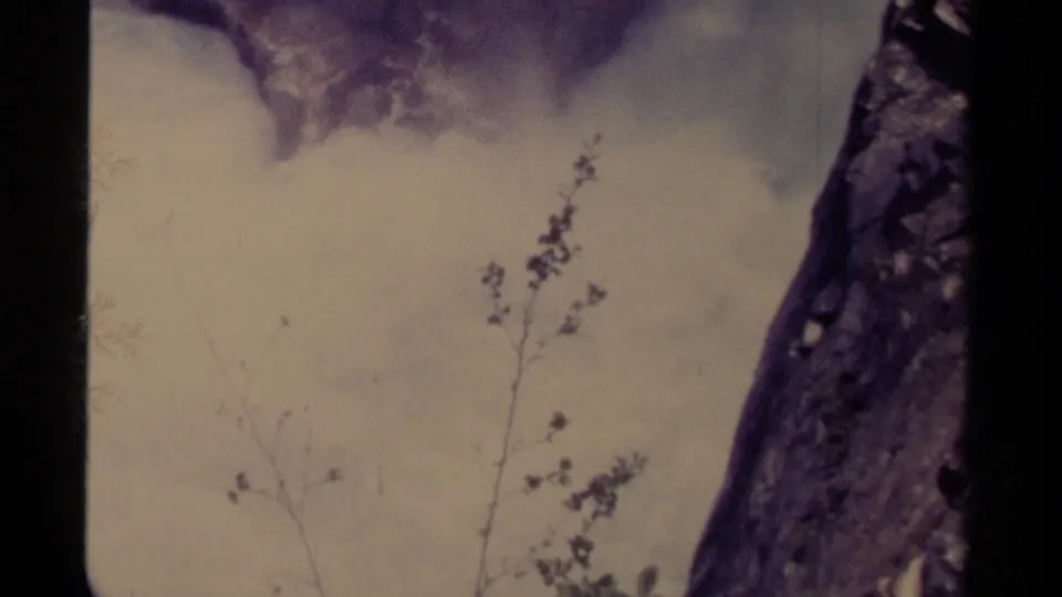 1979 Canada 8mm frame showing waterfall spray and mist behind thin branches, with a dark rock wall at right and aged film borders.