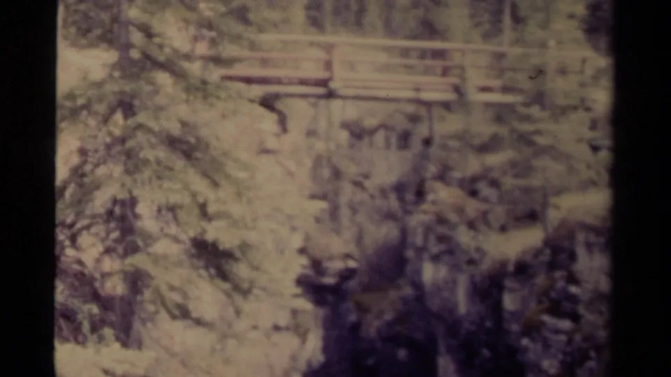 Faded 1979 8mm Canada frame with a wooden bridge crossing a tree-lined rocky ravine.