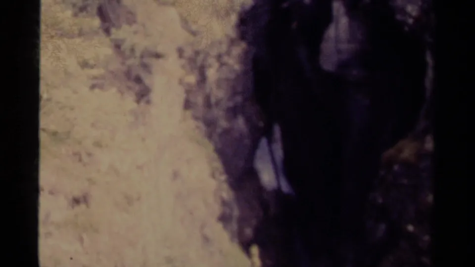 Canadian 1979 8mm frame showing the lower section of a shadowed waterfall amid rocks, trees, and faded color.