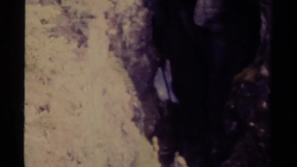 1979 Canadian 8mm still showing a narrow waterfall running through a shaded mountain canyon with forest at the edge.