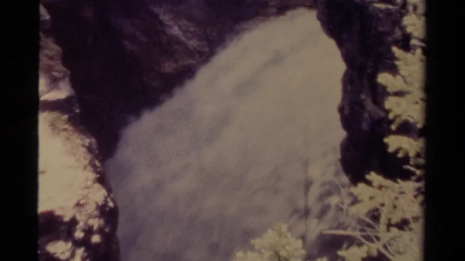 1979 Canadian home-movie frame showing water surging through rocks with sparse vegetation near the channel.