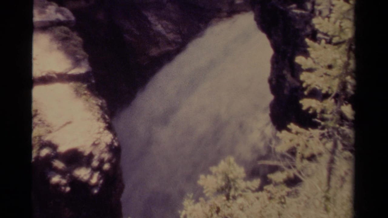 Waterfall rushing between dark rocks with vegetation at the canyon edge.