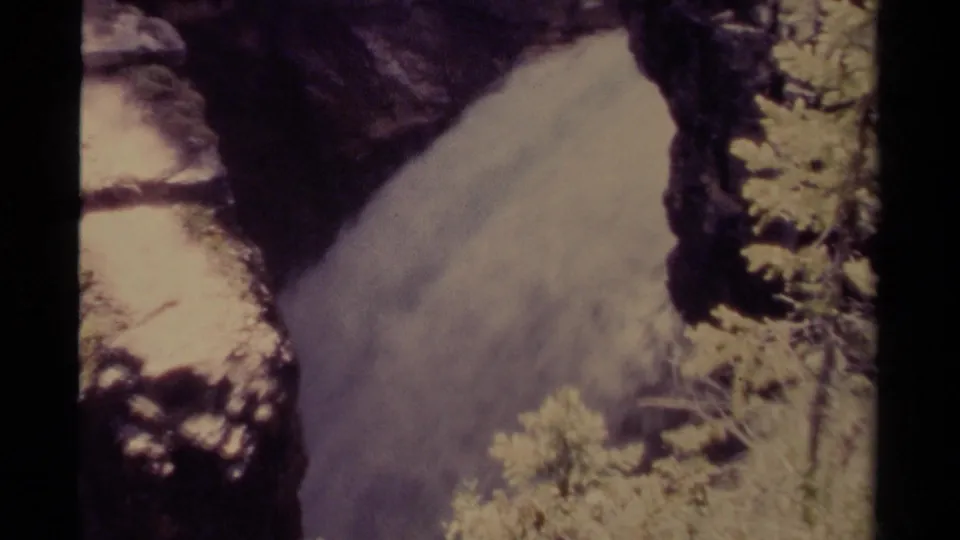 1979 Canadian 8mm frame of a waterfall dropping through dark canyon rock, partly framed by pale vegetation.