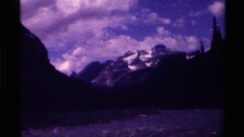 1979 Canada 8mm frame with mountain slopes, snow highlights, dense clouds, and a dark possible water surface in the foreground.