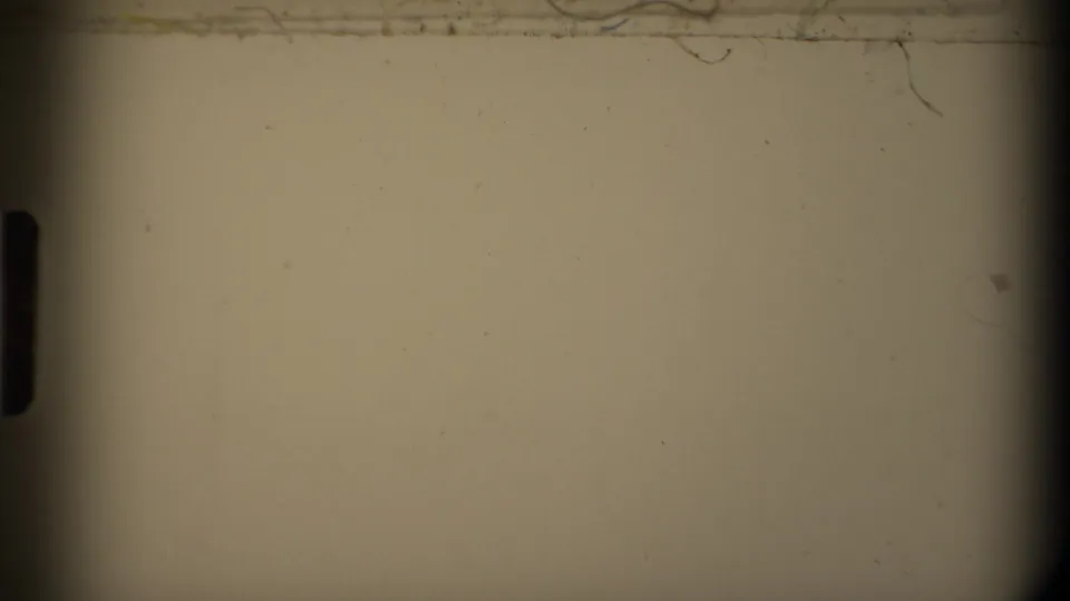 A pale transitional 8mm frame with film edge shadow, scratches, dust, and little readable scene detail.