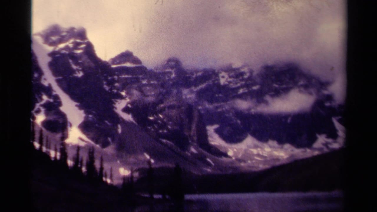 Snow-streaked mountain peaks above a dark tree line and lake edge.