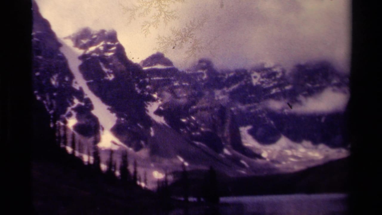 Rocky snow-covered peaks with cloud cover and a dark lake shoreline.