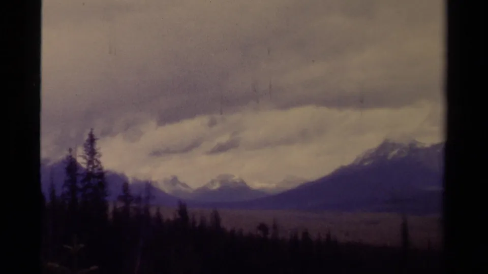 A 1979 8mm view of Canadian mountains partly framed by conifers, with visible gate edge and muted color shift.