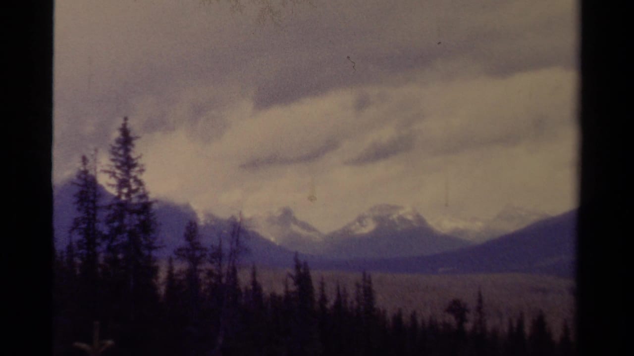 1979 8mm Canada view of evergreen silhouettes and snow-dusted mountains under thick cloud cover.