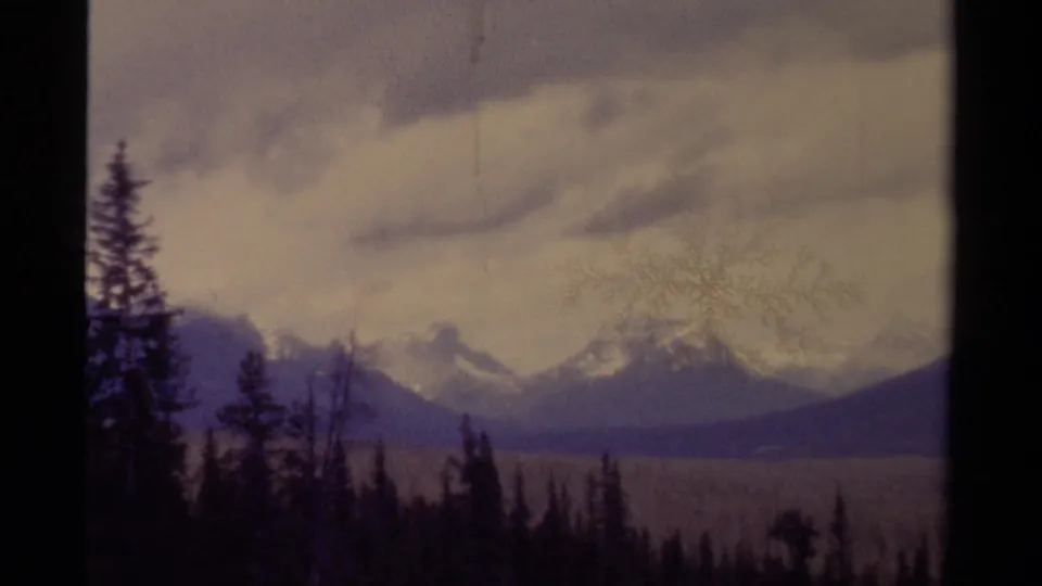 1979 8mm Canada frame with soft-focus mountains, dark tree silhouettes, and visible film wear.