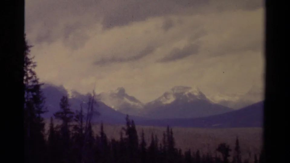 1979 8mm Canada landscape frame showing a forested foreground, distant snowy peaks, and muted cloudy light.