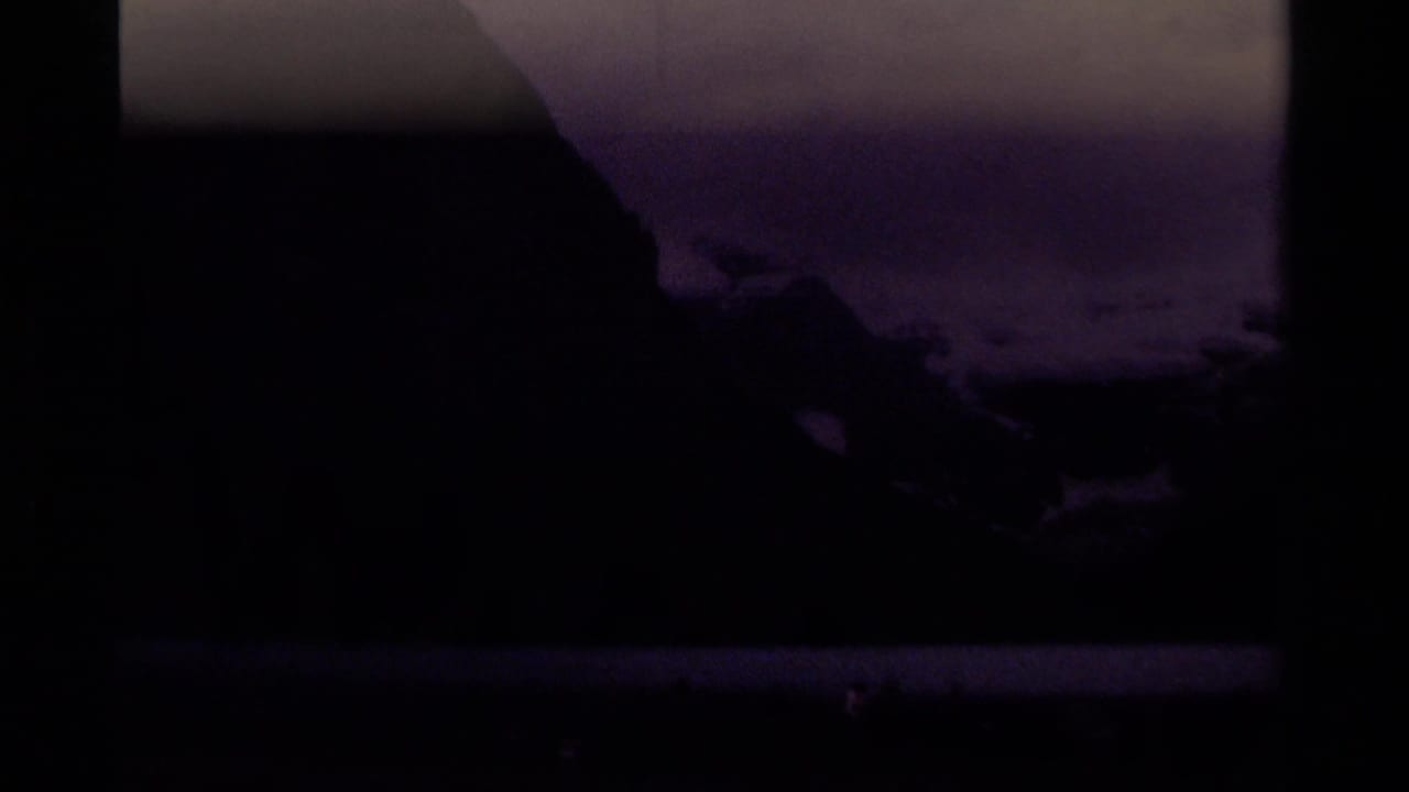 Dark mountain lake landscape with snowy peaks under a cloudy sky.