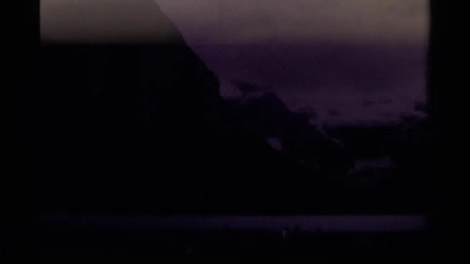 1979 8mm Canadian mountain lake view with dark slopes, snow patches, heavy clouds, and visible film-frame edges.