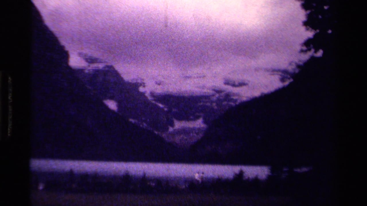 1979 Canadian mountain-lake view on 8mm film, with distant walkers along the shoreline under a purple cloudy sky.