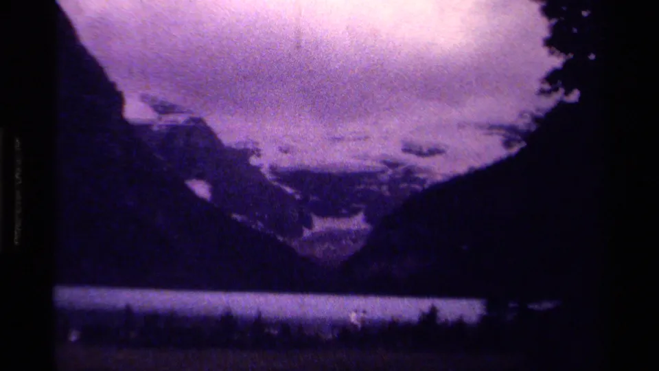 1979 Canadian mountain-lake view on 8mm film, with distant walkers along the shoreline under a purple cloudy sky.