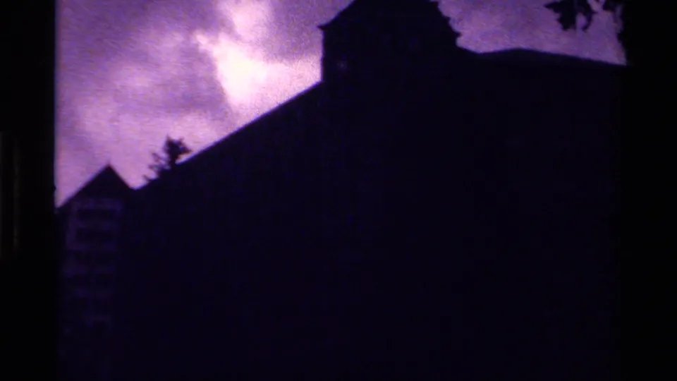 1979 Canada 8mm frame showing a large building partly in silhouette, with pine trees and a bright purple-shifted sky.