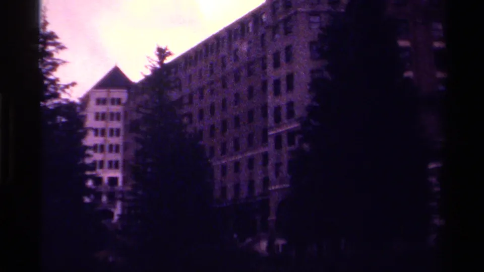 1979 Canada 8mm frame showing a large building facade, peaked roof section, trees, and a dark waterfront or shoreline foreground.