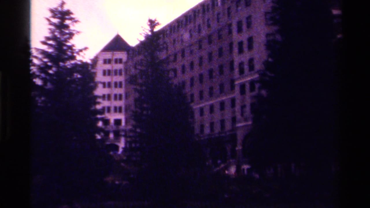 1979 Canadian 8mm frame showing a large hotel facade and tower partly obscured by evergreen trees.