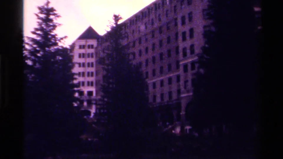 1979 Canadian 8mm frame showing a large hotel facade and tower partly obscured by evergreen trees.