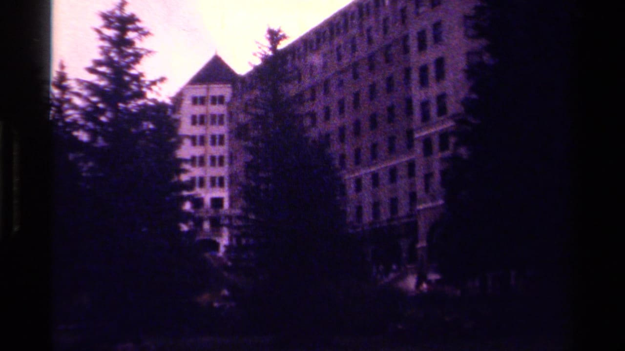 Visitor-shot 8mm view of a multi-story Canadian mountain hotel partly hidden by trees.