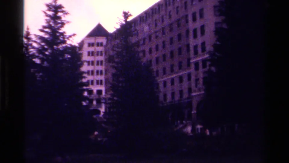 1979 home-movie frame of a tall hotel structure behind evergreens, with soft focus and faded color.