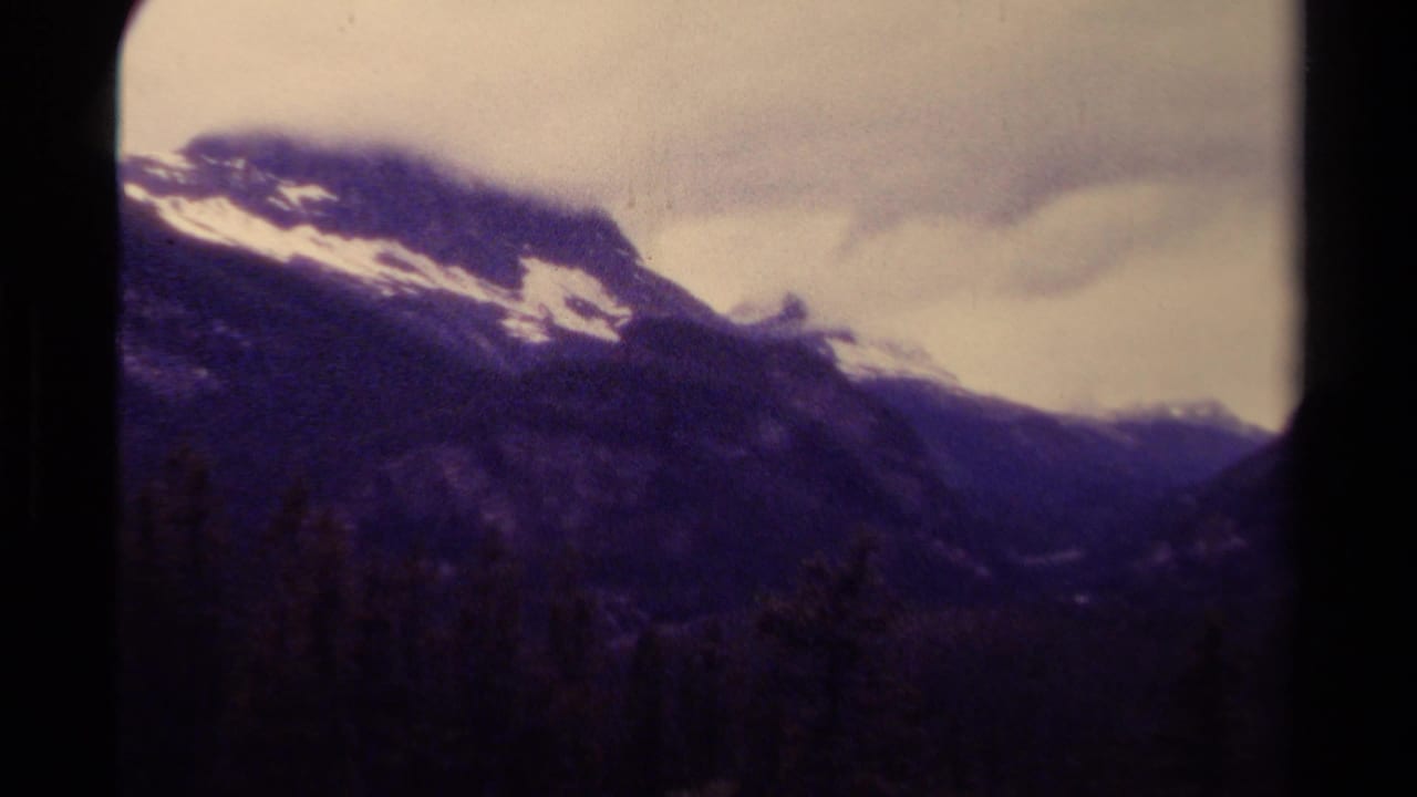 1979 Canadian 8mm frame showing a snow-streaked mountain ridge, dark forested valley, and soft cloud cover.