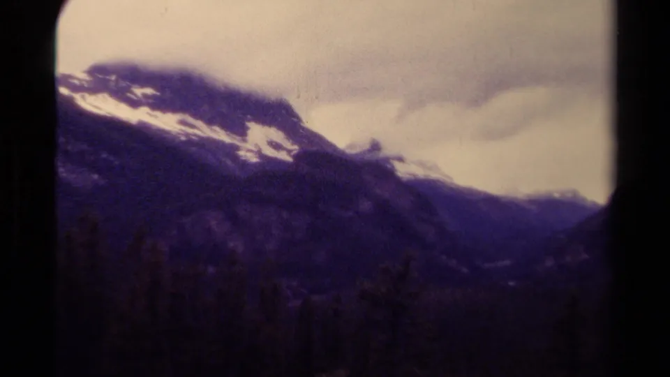 1979 Canadian 8mm frame showing a snow-streaked mountain ridge, dark forested valley, and soft cloud cover.