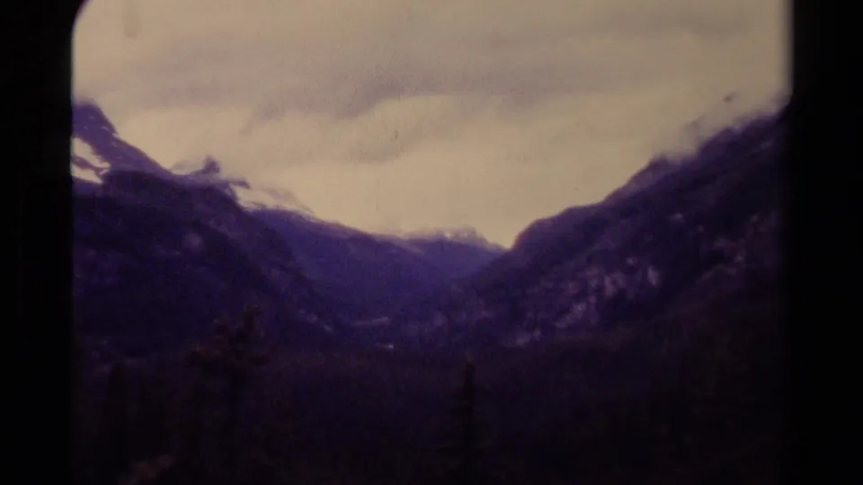 1979 Canadian 8mm frame showing a mountain valley between dark slopes with muted clouds and aged film color.