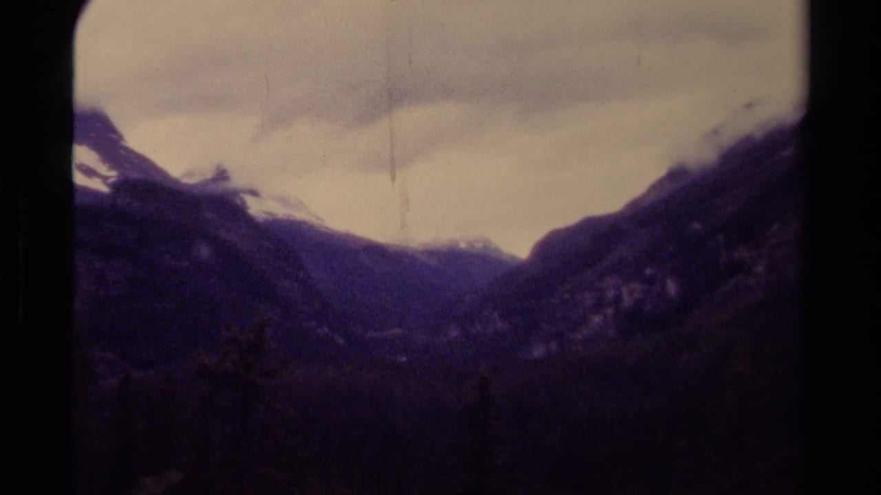 1979 8mm Canada footage showing a misty mountain valley, dark evergreen forest, snow-dusted peaks, and cloudy winter light.