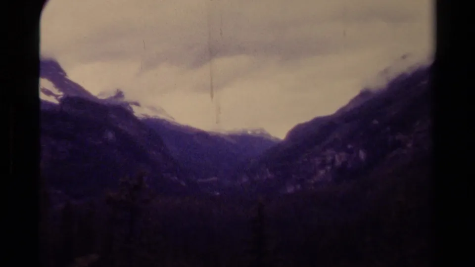 1979 8mm Canada footage showing a misty mountain valley, dark evergreen forest, snow-dusted peaks, and cloudy winter light.