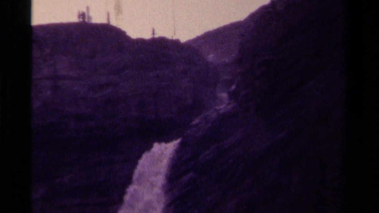 1979 Canadian 8mm frame with a waterfall glimpsed between rugged mountain slopes under a pale sky.