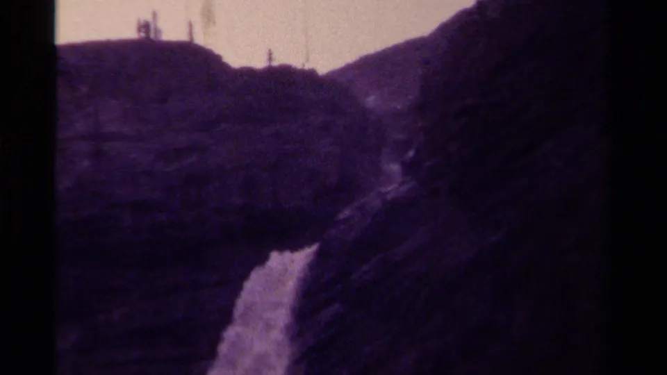 1979 Canadian 8mm frame with a waterfall glimpsed between rugged mountain slopes under a pale sky.