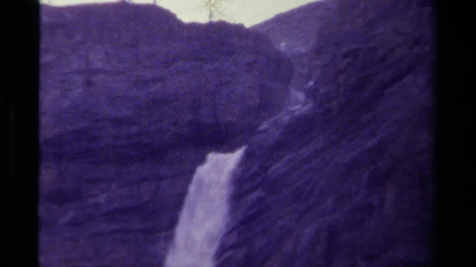 1979 Canadian 8mm frame showing a distant waterfall dropping through a rugged mountain ravine with soft grain and purple cast.