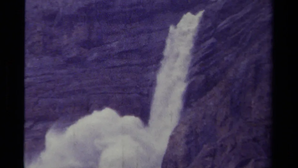 1979 8mm Canada footage showing a waterfall plunging down a rugged dark cliff with mist gathering below.