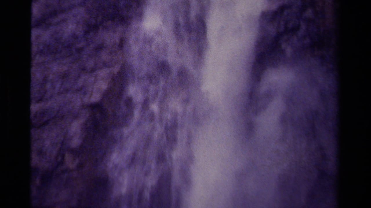 Tall waterfall descending over a rocky cliff with a strong purple film cast.