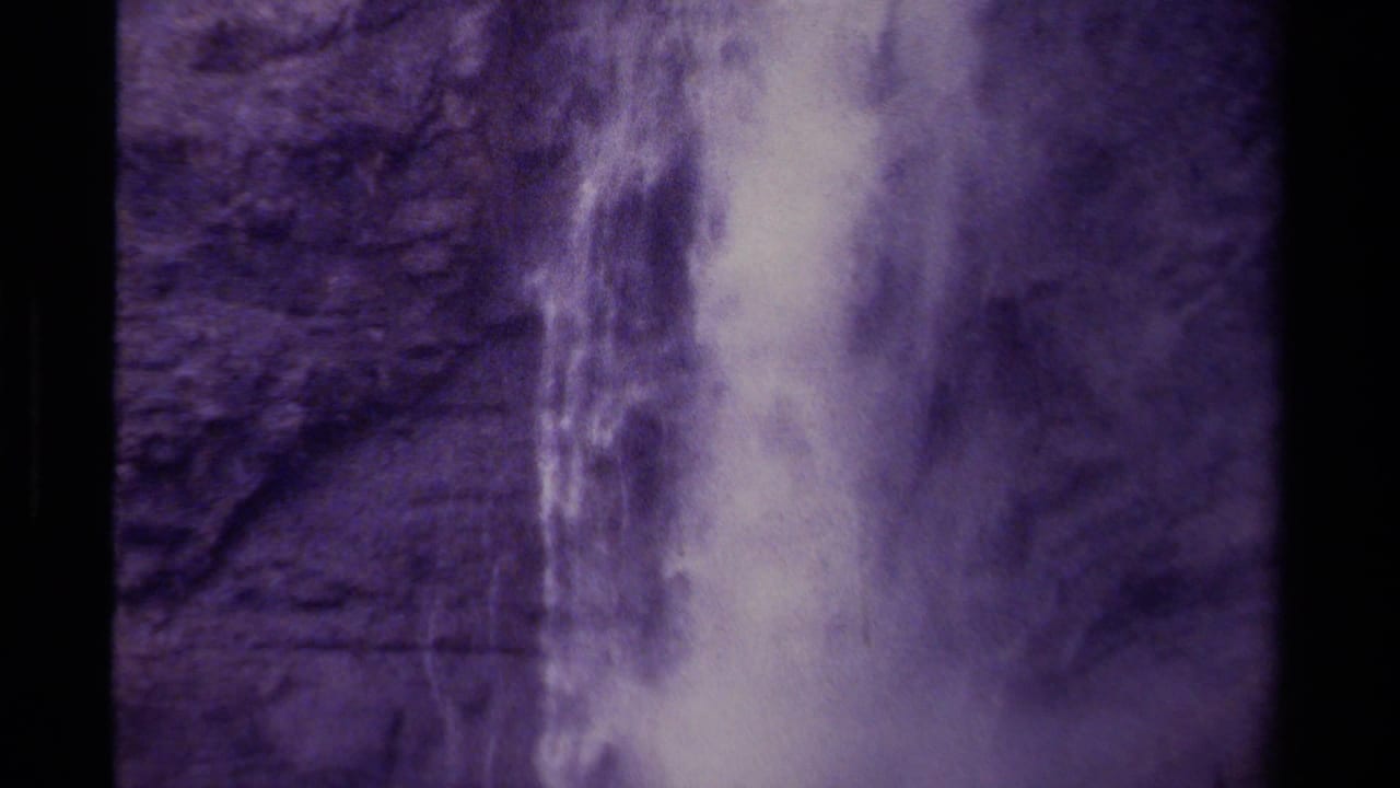 Waterfall spilling down a rough cliff face, framed by dark film edges.