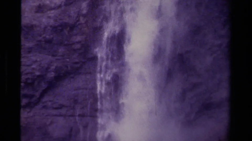 1979 Canadian home-movie frame with the waterfall centered against rugged rock, showing grain, muted contrast, and film-edge darkness.