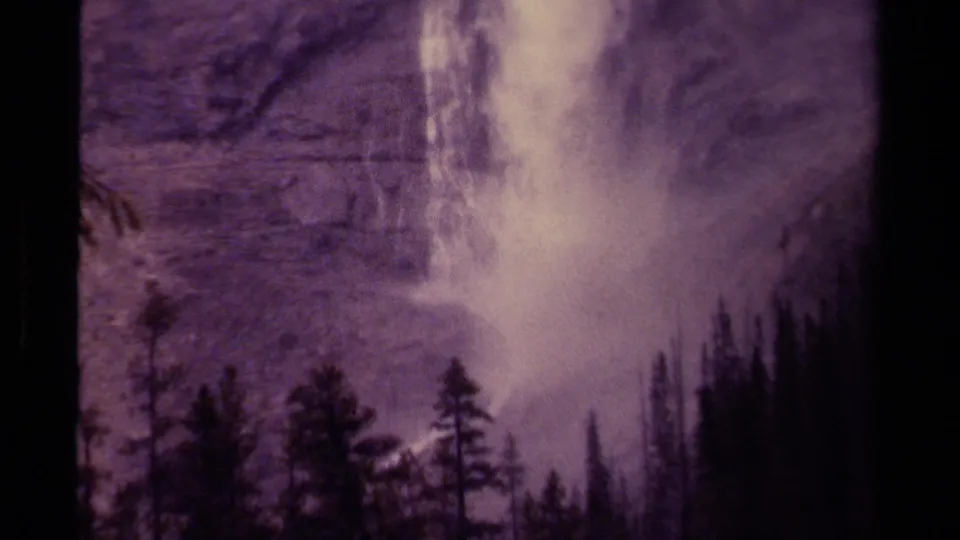 1979 Canadian 8mm frame showing the lower waterfall, mist, rocky slope, and dark evergreen silhouettes in the foreground.