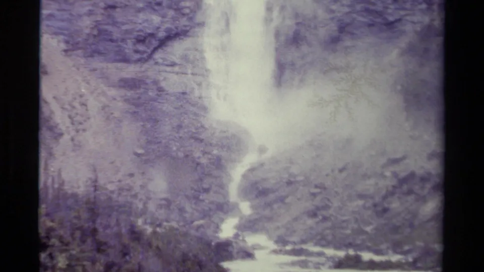 1979 Canadian home-movie frame showing the bright lower cascade, stream channel, rocky terrain, and pale overexposed film texture.