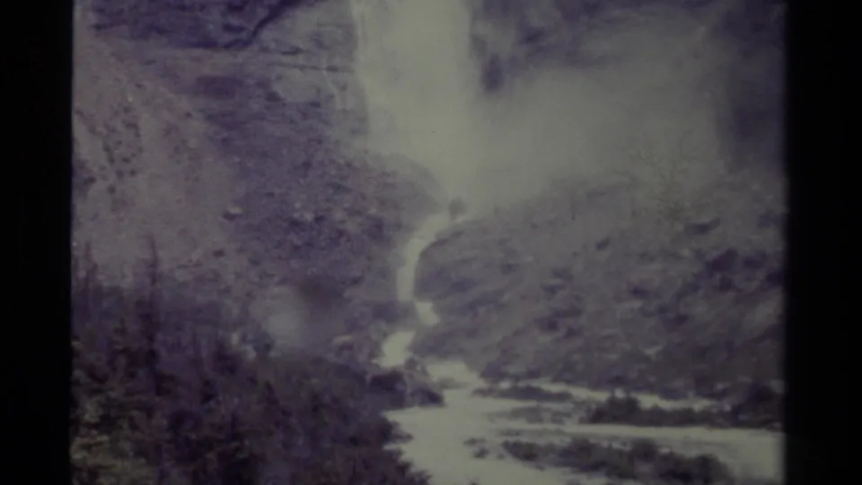1979 Canadian home-movie frame of a waterfall feeding a bright stream through rugged terrain and trees.